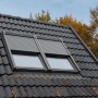 Solar Rollladen CK02 Alu für Dachfenster, teilweise geöffnet, auf dunklem Dach.