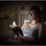 Frau liest mit Energizer Booklight LED-Taschenlampe im Bett. Leselampe mit flexiblem Hals.