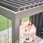 Biohort Pergola, 6x3,5m, dunkelgrau-silber, mit Lamellendach und Frau im Sessel.