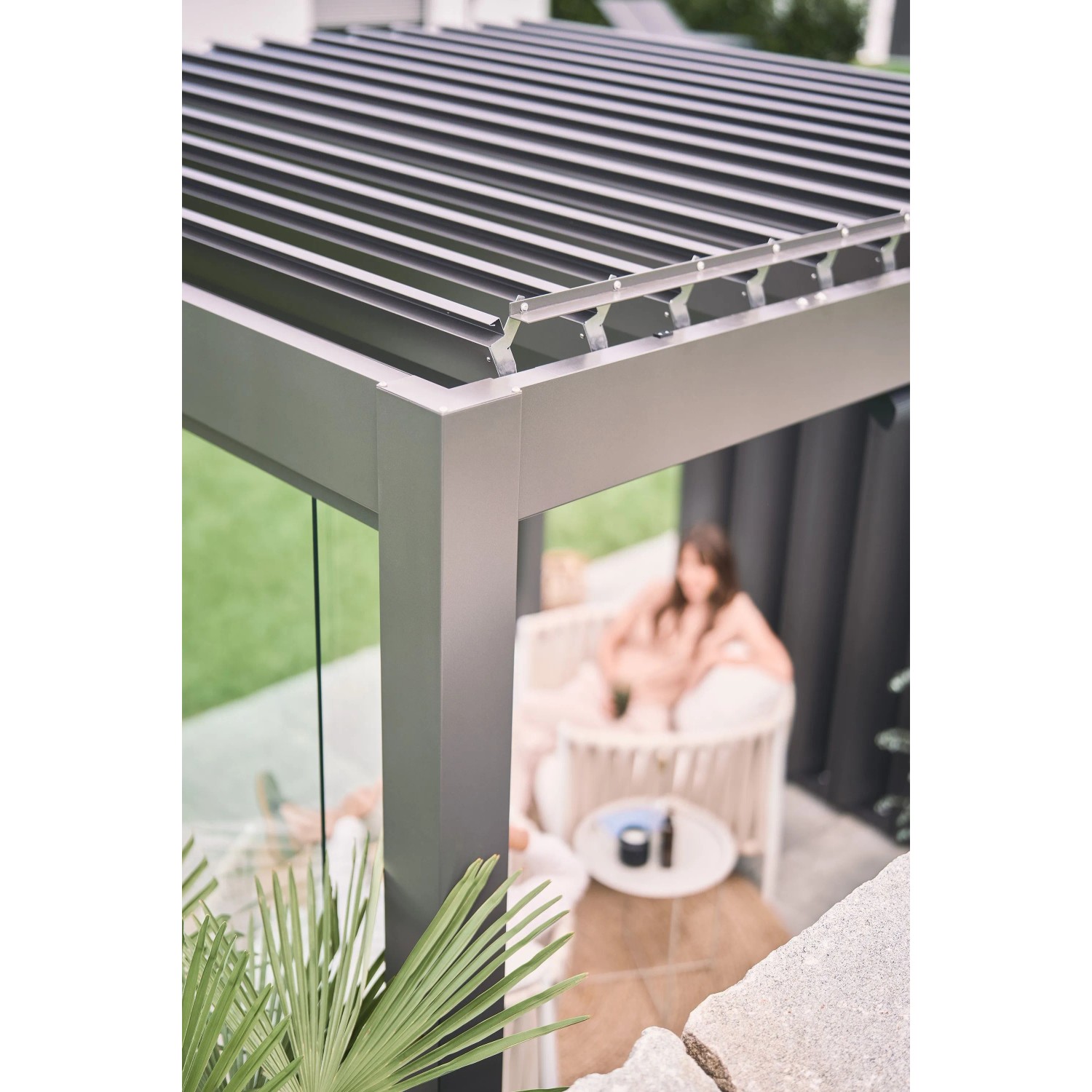 Biohort Pergola, 6x3,5m, dunkelgrau-silber, mit Lamellendach und Frau im Sessel.