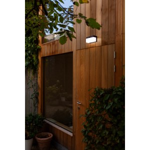 Schwarze, eckige Lutec LED Solar Wandleuchte Fran an einer Holzwand. Moderne Außenleuchte mit Bewegungsmelder.