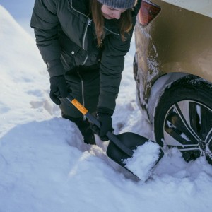 Orange-schwarze Fiskars Autoschaufel Plus beim Schneeräumen neben einem Auto.