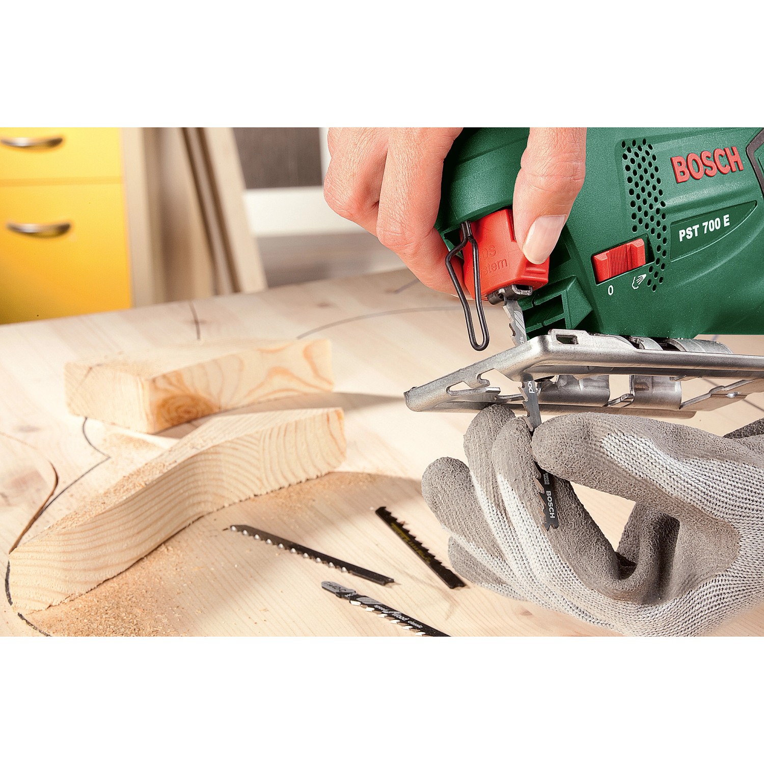 Bosch PST 700 E Stichsäge in Aktion beim Holzsägen, mit Sägeblättern auf Werkbank.