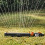Fiskars Viereckregner On/Off in Aktion: Oszillierender Sprinkler bewässert Rasenfläche.
