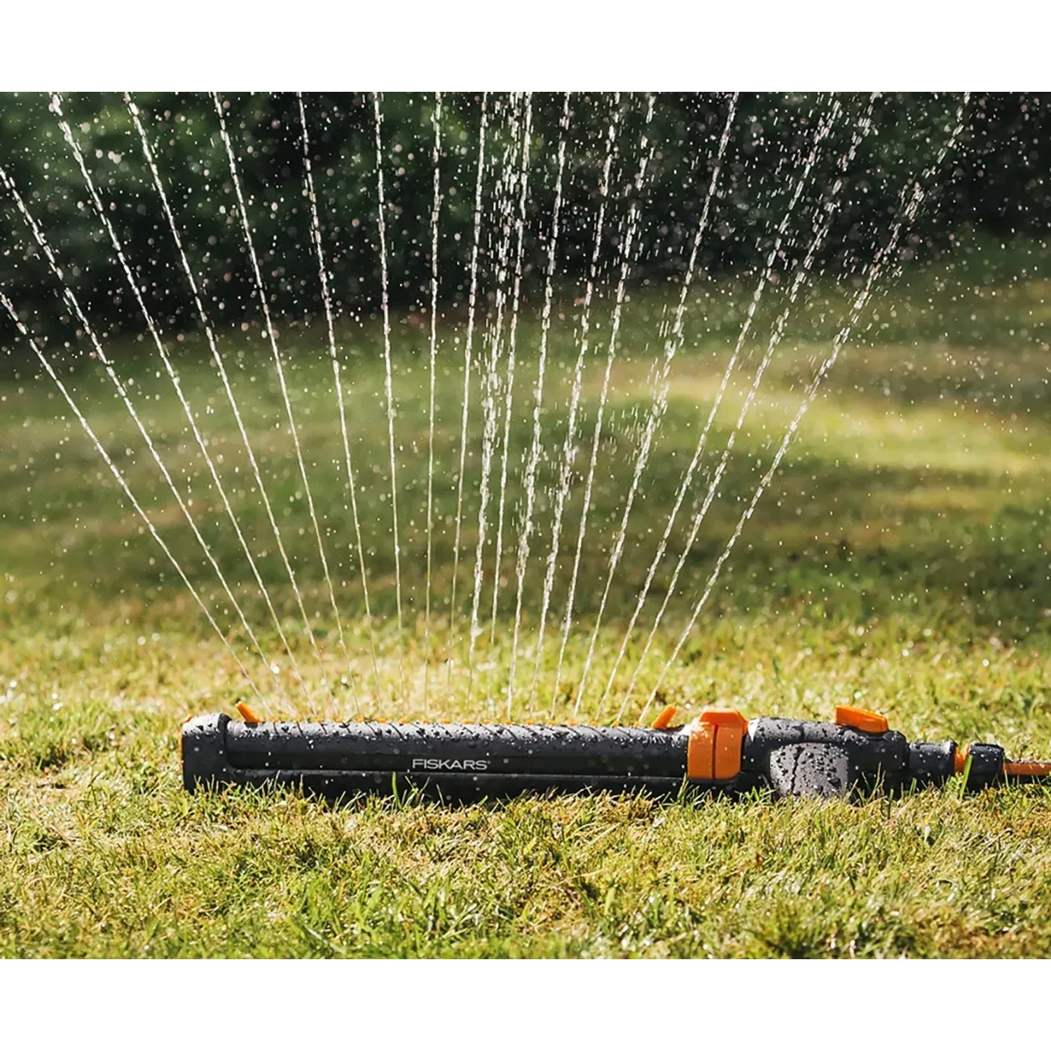 Fiskars Viereckregner On/Off in Aktion: Oszillierender Sprinkler bewässert Rasenfläche.