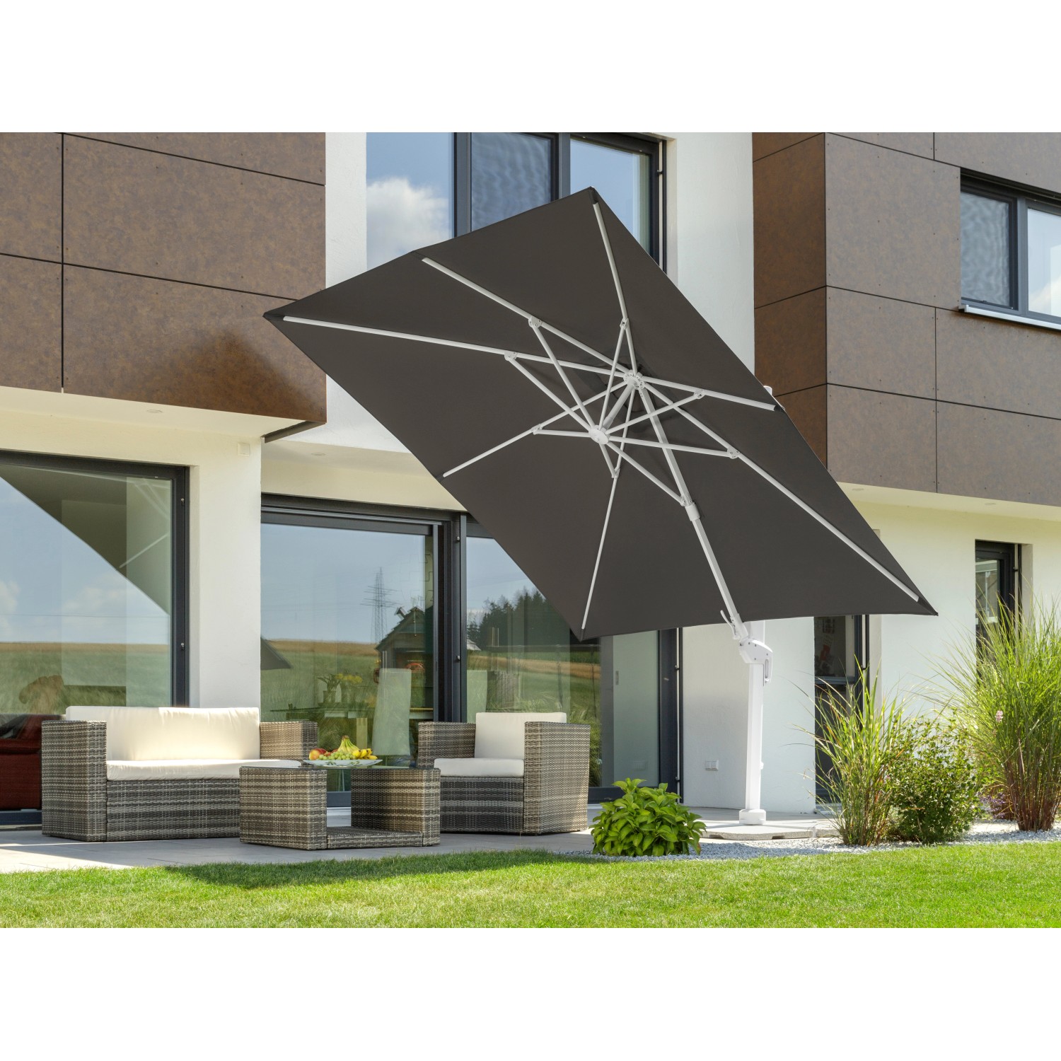 Anthrazitfarbener Schneider Ampelschirm Rhodos 360 cm mit Kurbel über Lounge-Set im Garten.