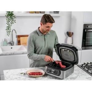 Ninja Foodi Grill AG301EU: Mann legt Steak auf den geöffneten Grill. Küchenmaschine in Grau-Schwarz.