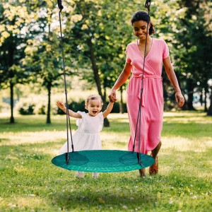 Mutter führt Kind zur grünen Nestschaukel im Garten. Spielturm Zubehör für Kinder.