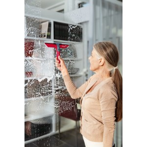 Frau reinigt Fenster mit Vileda Profi-Fensterwischer Handgerät. Reinigungsgerät mit rotem Griff.
