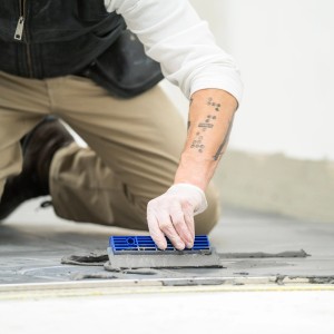 Handwerker verteilt Mapei Fliesenkleber C2TE mit einer Zahnspachtel auf dem Boden.