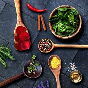 Glasbild Kochkreation, 30x30 cm: Arrangement aus Gewürzen und Kräutern in Holzlöffeln.