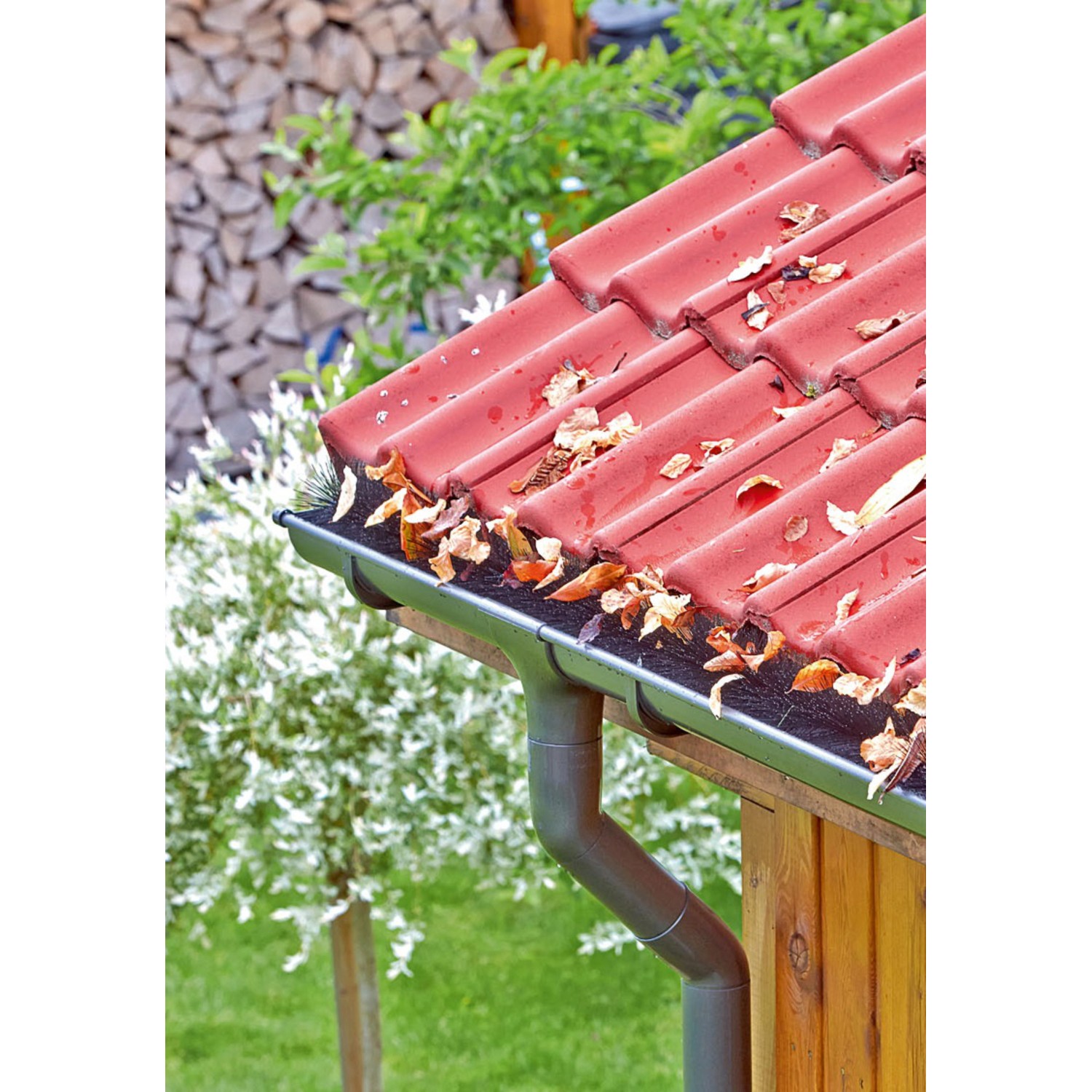 Verstopfte Dachrinne mit Laub unter rotem Ziegeldach. Marley Rinnenraupe schützt vor Verschmutzung.