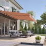 Beige-rote Gelenkarmmarkise Wismar Classic, 300x200 cm, montiert an Hauswand über Terrasse.