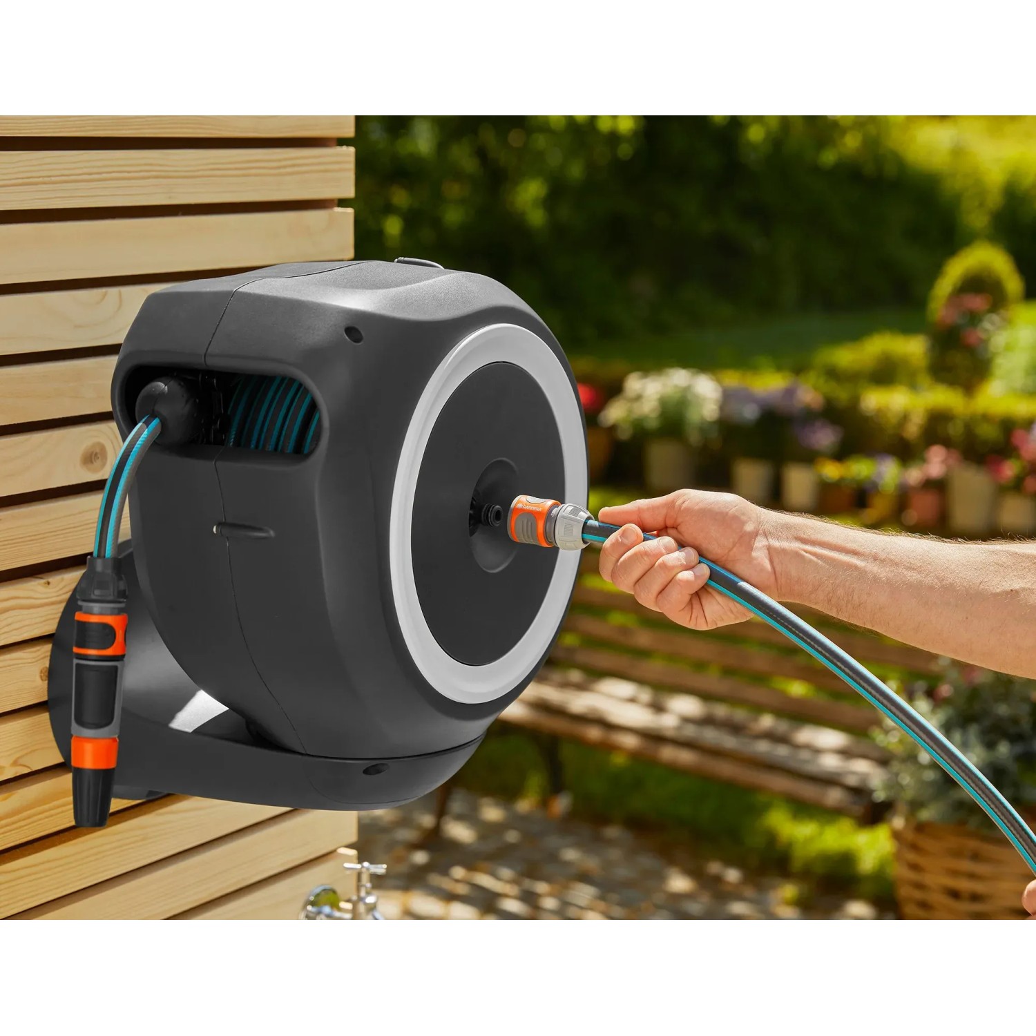 Gardena Wand-Schlauchbox RollUp S mit 15 m Schlauch im Einsatz, montiert an einer Holzwand.