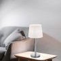 Trio Tischleuchte Lyon, Nickel matt, mit weißem Stoffschirm auf kleinem Holztisch.