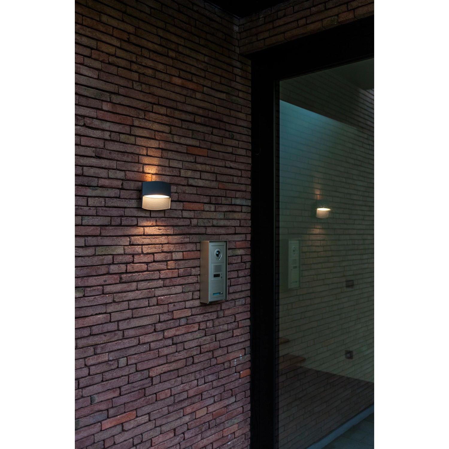 Anthrazitfarbene Lutec LED-Außenwandleuchte Lotus mit Up & Down Lichteffekt an einer Backsteinwand.