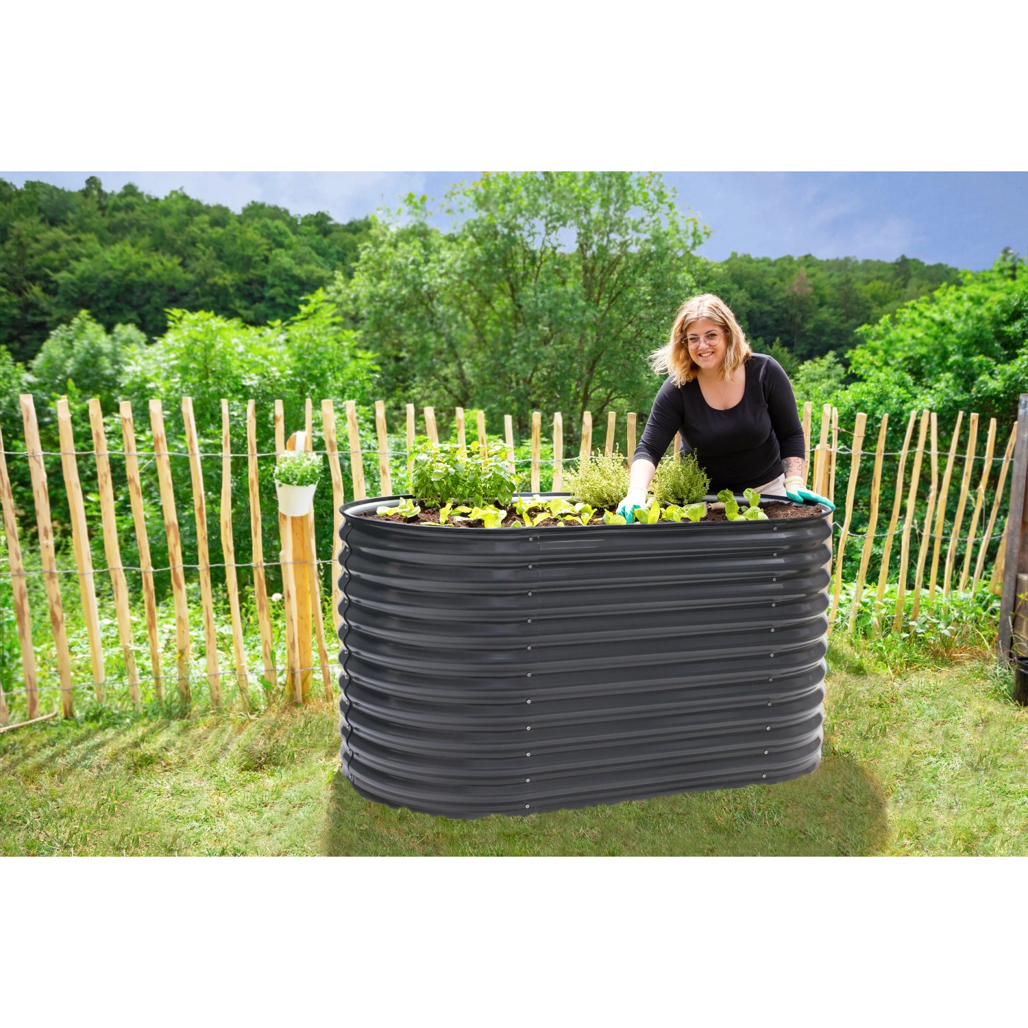 Ovales, anthrazitfarbenes Westmann Metall-Hochbeet (160x80x82cm) mit Bepflanzung und Frau im Garten.