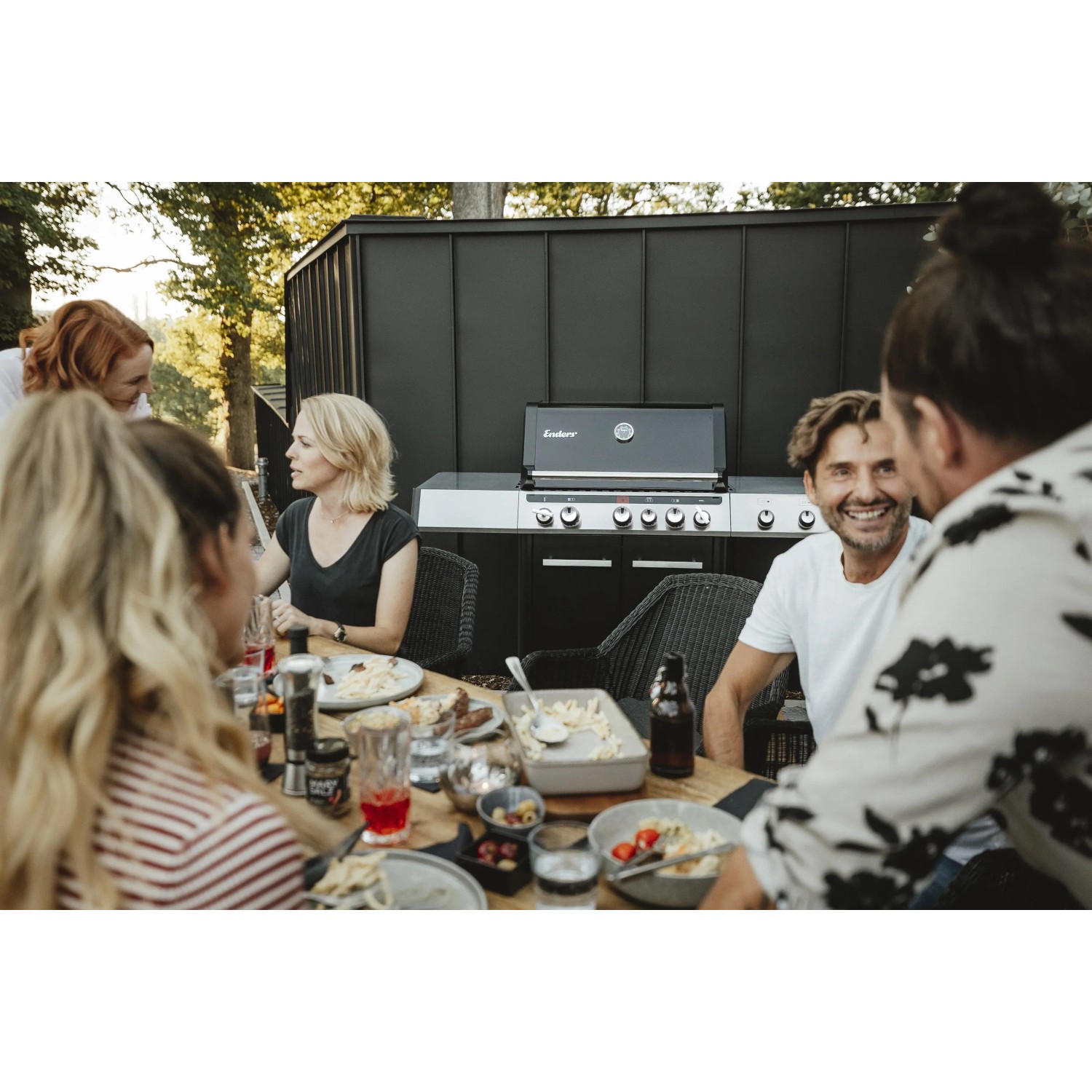 Enders Gasgrill Uniq Pro 3 IK Cruster in Schwarz-Edelstahl mit Personen beim Grillen.