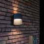 Moderne Lutec LED-Außenwandleuchte Lotus in Anthrazit mit Up & Down Lichteffekt an einer Backsteinwand.
