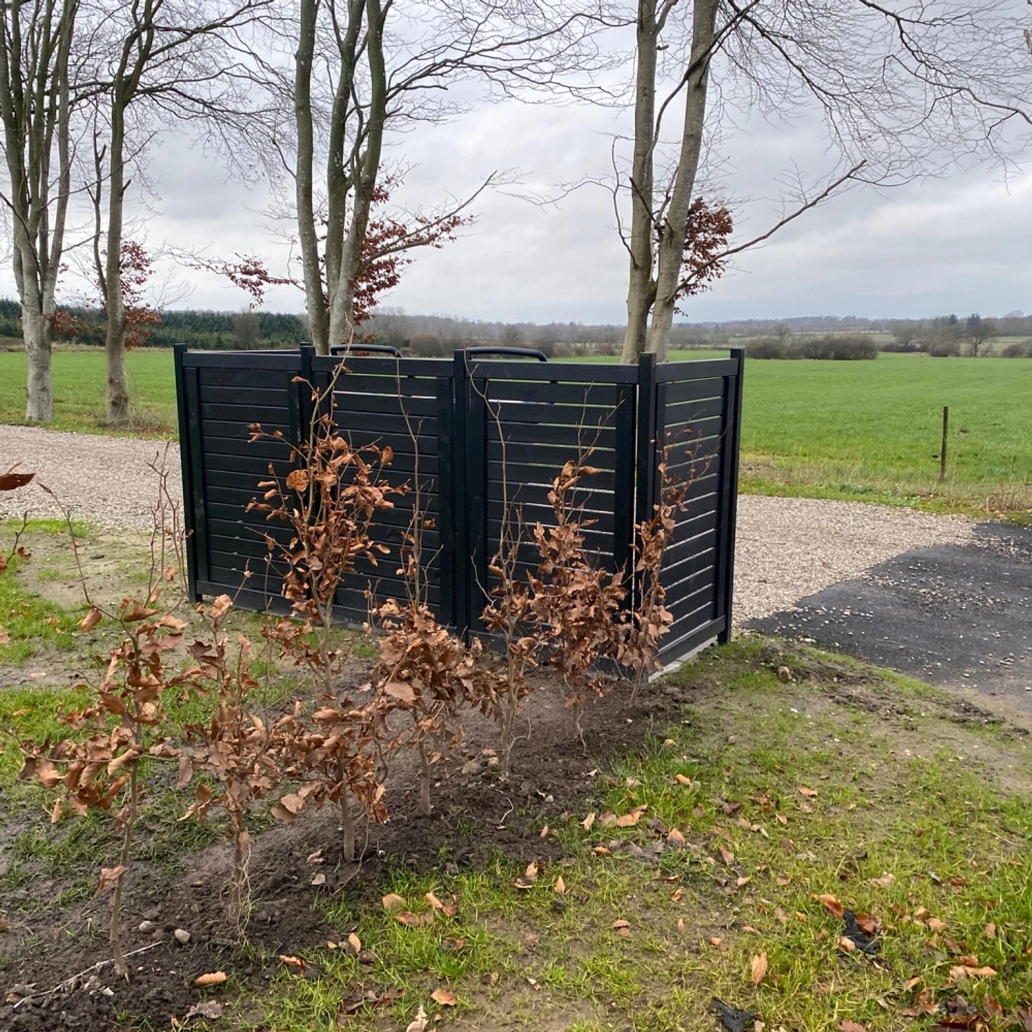 Schwarze Mülltonnenverkleidung Lund (245x85x124cm) im Garten. Sichtschutz für Mülltonnen.