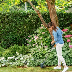 Frau trimmt Rasen mit Bosch Akku-Rasentrimmer EasyGrassCut 18-230 im Garten.