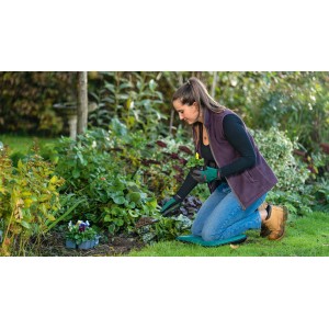 Frau pflanzt Blume mit Bosch Garten-Pflanzkelle im Garten. Kategorie: Gartenhandgeräte.