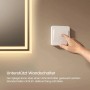 Hand schaltet Emke Badspiegel mit warmweißer LED-Beleuchtung über Wandschalter ein. Komfortable Bedienung im Bad.