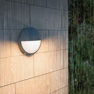 Anthrazitfarbene Philips Capricorn LED Außenwandleuchte mit warmweißem Licht an einer Hauswand im Regen.