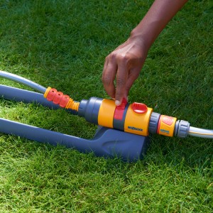 Hozelock Rasensprenger AquaSave Pro 220 in Nutzung: Hand reguliert Wasserdurchfluss auf Rasen.