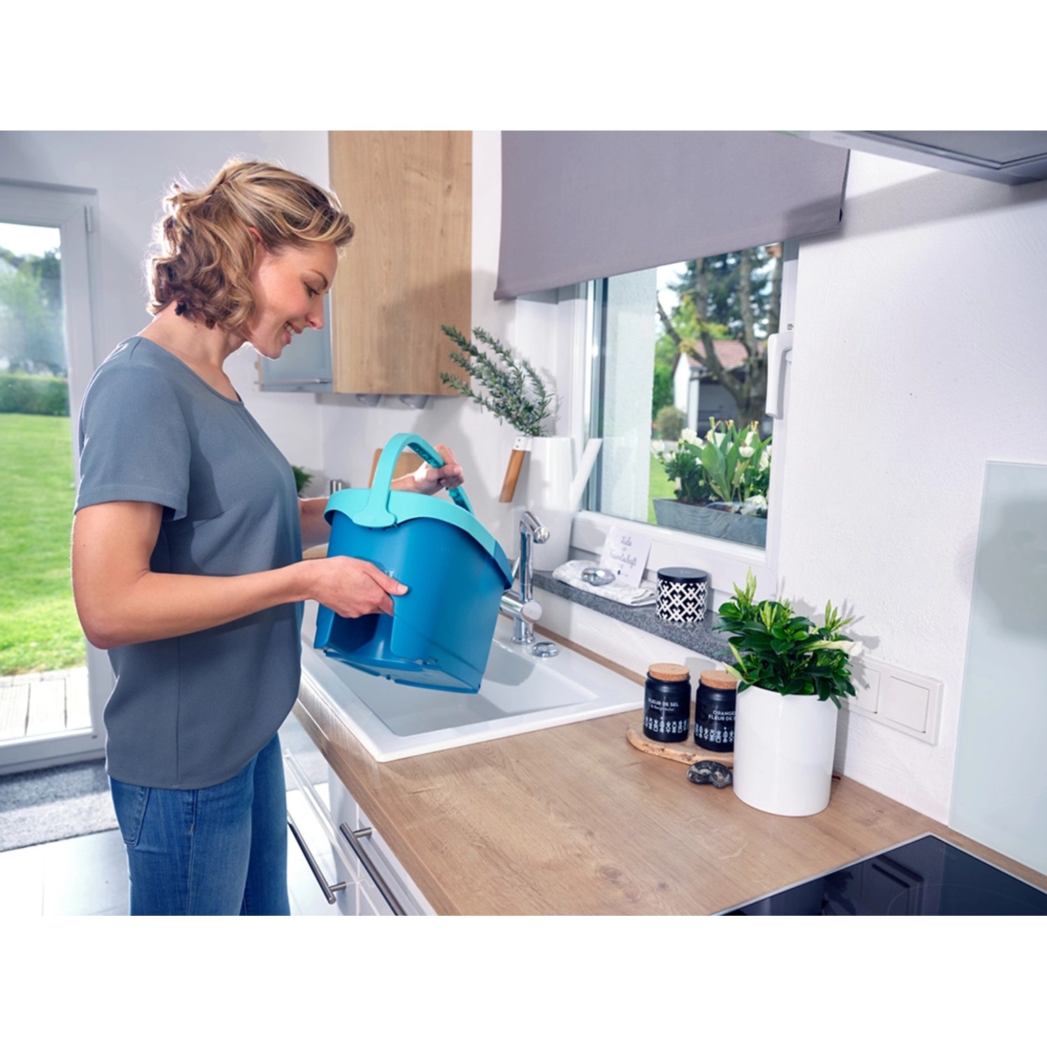 Frau befüllt blauen Leifheit Clean Twist Disc Mop Ergo Eimer am Waschbecken. Reinigungsgeräte Set.