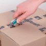Hand schneidet Paket mit wolfcraft Sicherheits-Trapezklingen-Messer. Kunststoffgehäuse.