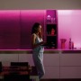 Frau in Küche mit Philips Hue Lightstrip White & Color Ambience LED-Streifen, der farbiges Licht spendet.