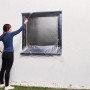 Frau deckt Fenster mit Tesa Abdeckfolie Easy Cover Outdoor ab. Schutz vor Farbe bei Aussenarbeiten.