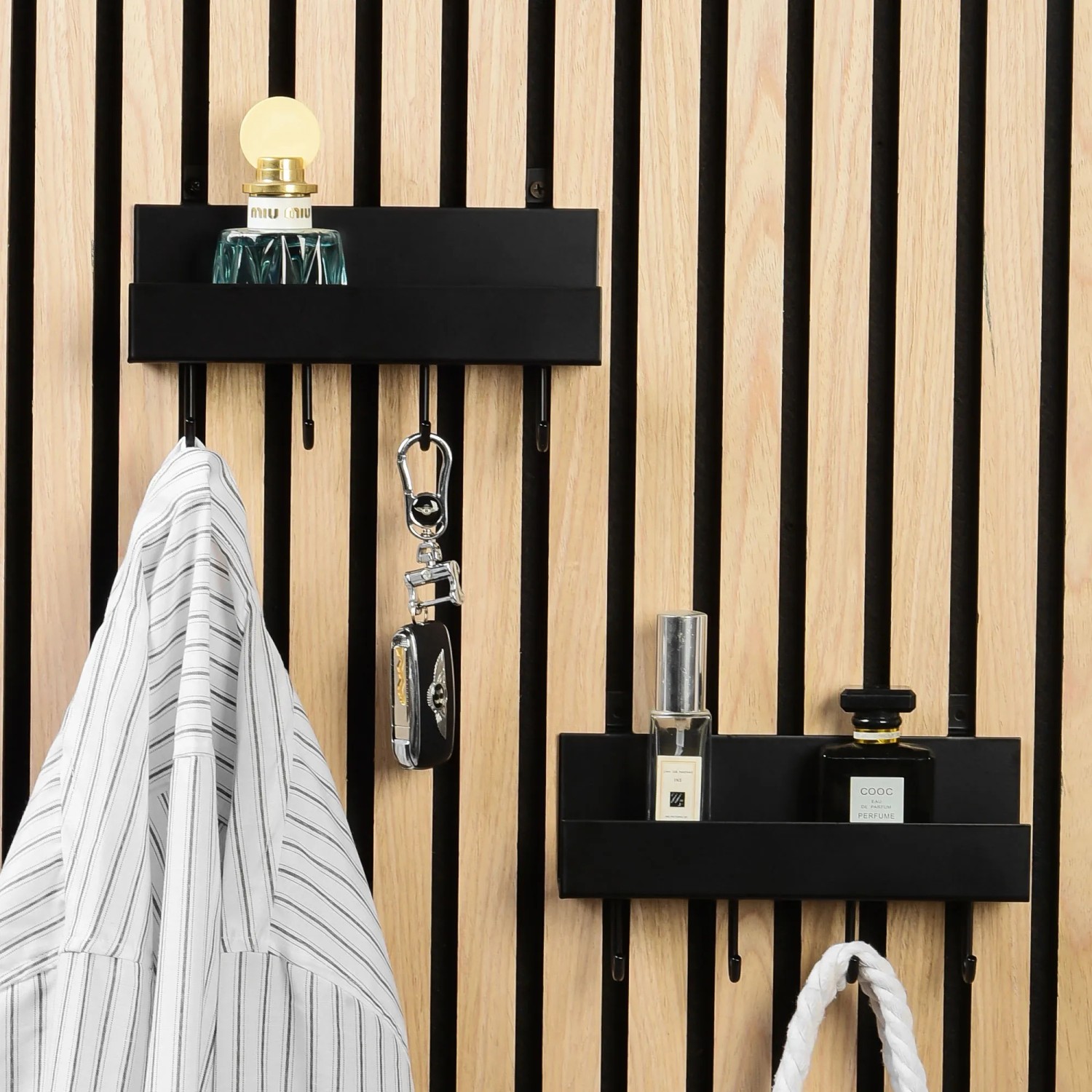 Schwarzes DenPanels Regal mit 4 Stiften an Akustikpaneel mit Deko und Jacke.
