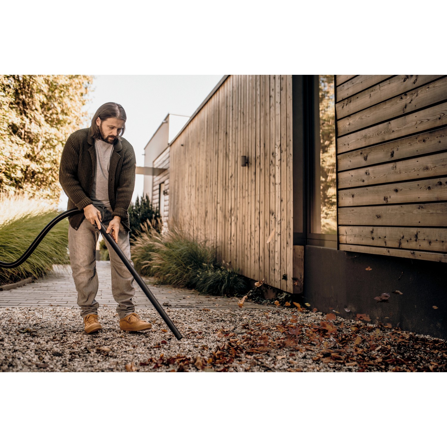 Mann nutzt Kärcher WD 2 Plus Nass-Trockensauger zur Laubentfernung im Garten.