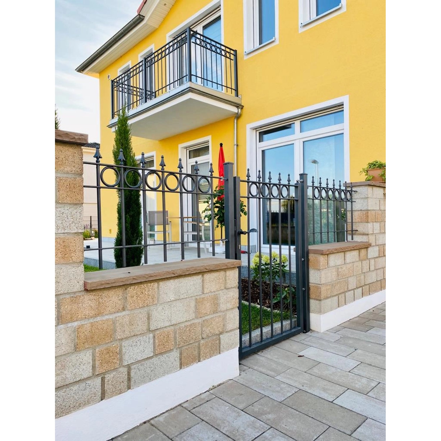 Eleo Zaun Belluno, pulverbeschichtet, 96 cm, vor gelbem Haus. Gartenzaun mit Kreisdekoren und Pinien-Spitzen.