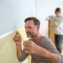 Mann klebt Tesa Malerband an Wand. Abdeckband für präzise Farbkanten bei Malerarbeiten.