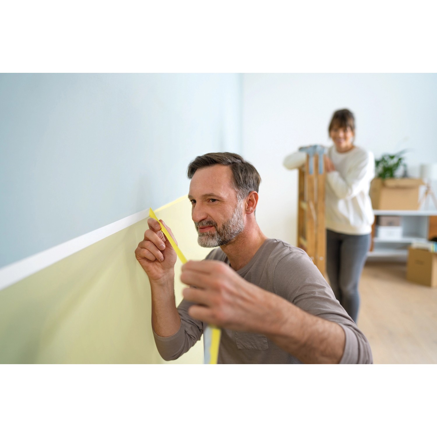 Mann klebt Tesa Malerband an Wand. Abdeckband für präzise Farbkanten bei Malerarbeiten.
