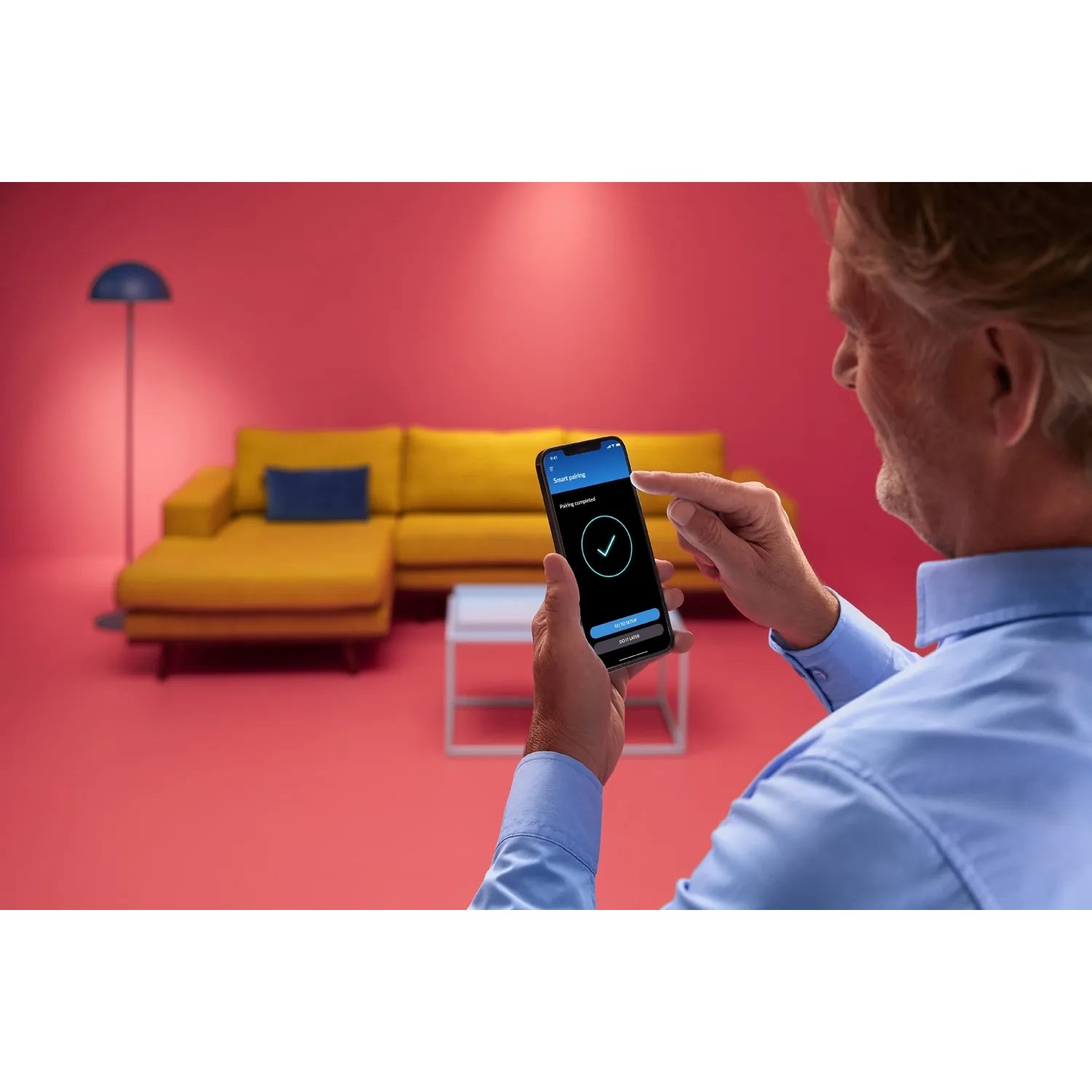 Mann steuert WiZ LED Stehleuchte per App. Smarte Lampe mit Farbwechsel für Wohnraum.