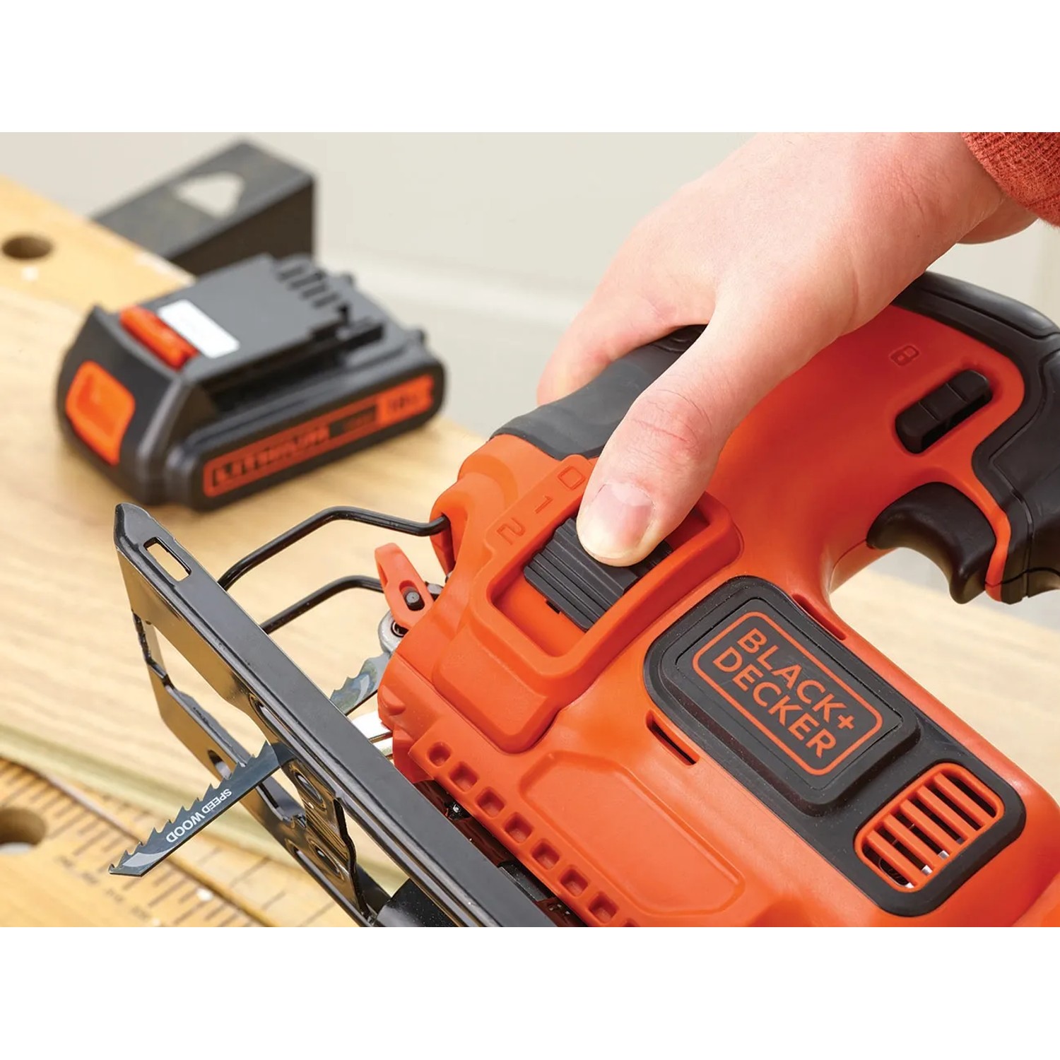 Black+Decker Akku-Stichsäge BDCJS18 in Aktion, mit Akku im Hintergrund.