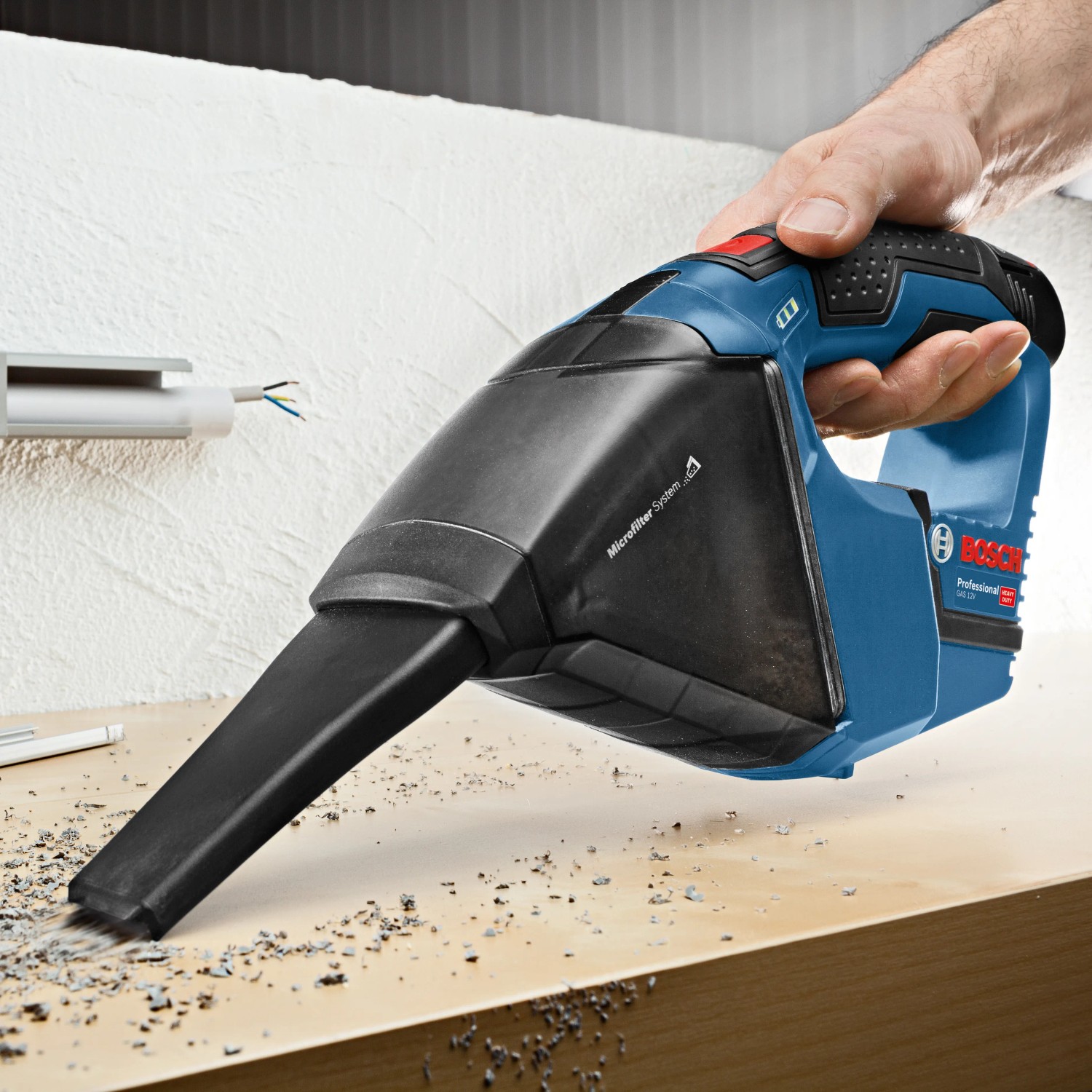 Bosch Professional GAS 12 V-LI Akku-Handstaubsauger im Einsatz beim Aufsaugen von Staub.