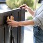 Person verstaut Gartenwerkzeug in Halterung der dunkelgrauen Biohort Gartenbox HighBoard. Praktische Aufbewahrung für Universalbox.