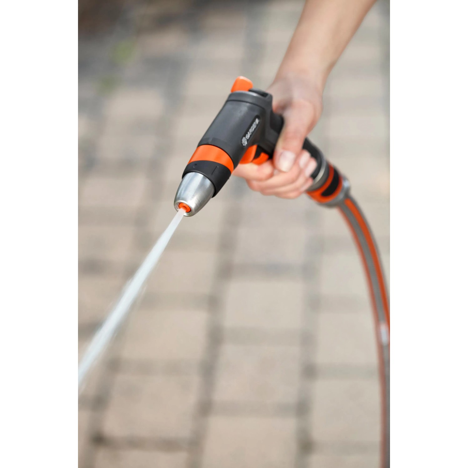 Hand hält Gardena Premium Reinigungsspritze mit Wasserstrahl. Gartenspritze für kraftvolle Reinigungsarbeiten.