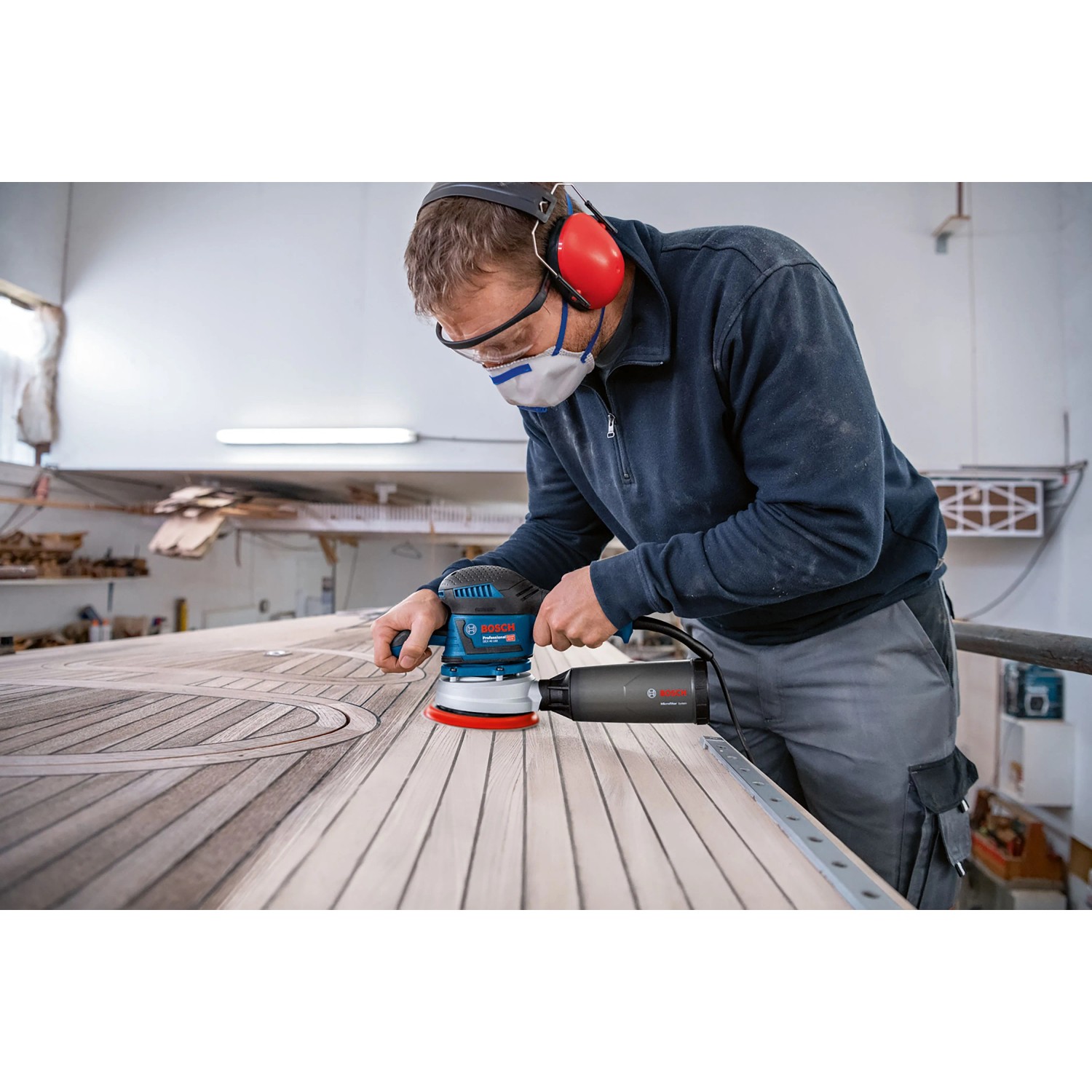 Mann schleift Holz mit Bosch Professional Exzenterschleifer GEX 40-150. Blaue Schleifmaschine mit rotem Schleifteller.
