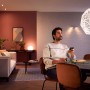 Mann steuert Philips Hue LED Lampe E27 in Wohnzimmer mit warmweißem Licht per App.
