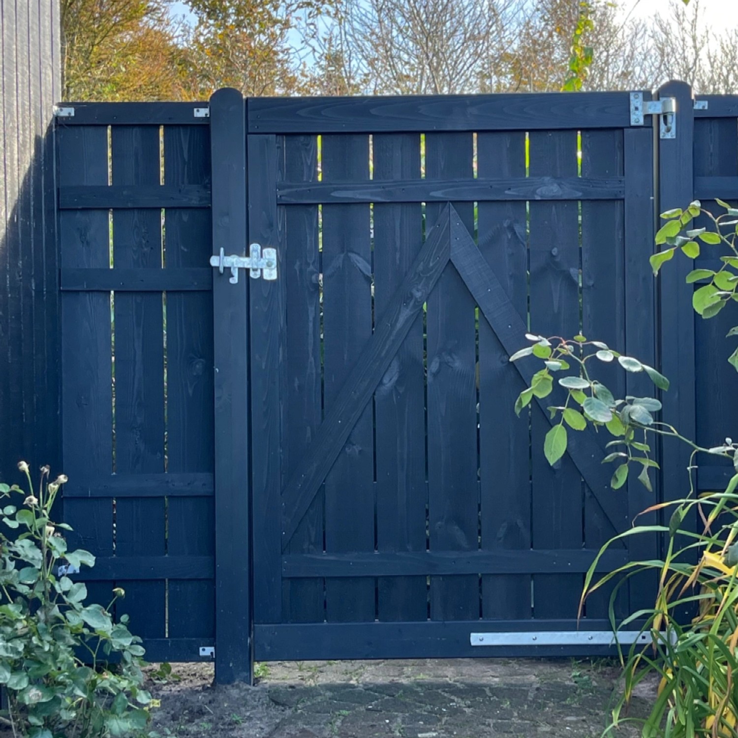 Schwarzer Sichtschutzzaun Rustik aus Nadelholz, 180x158 cm, mit Tür und silbernem Verschluss.