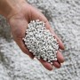 Hand hält Füllmaterial für Ecopots Pflanztopf, grau.