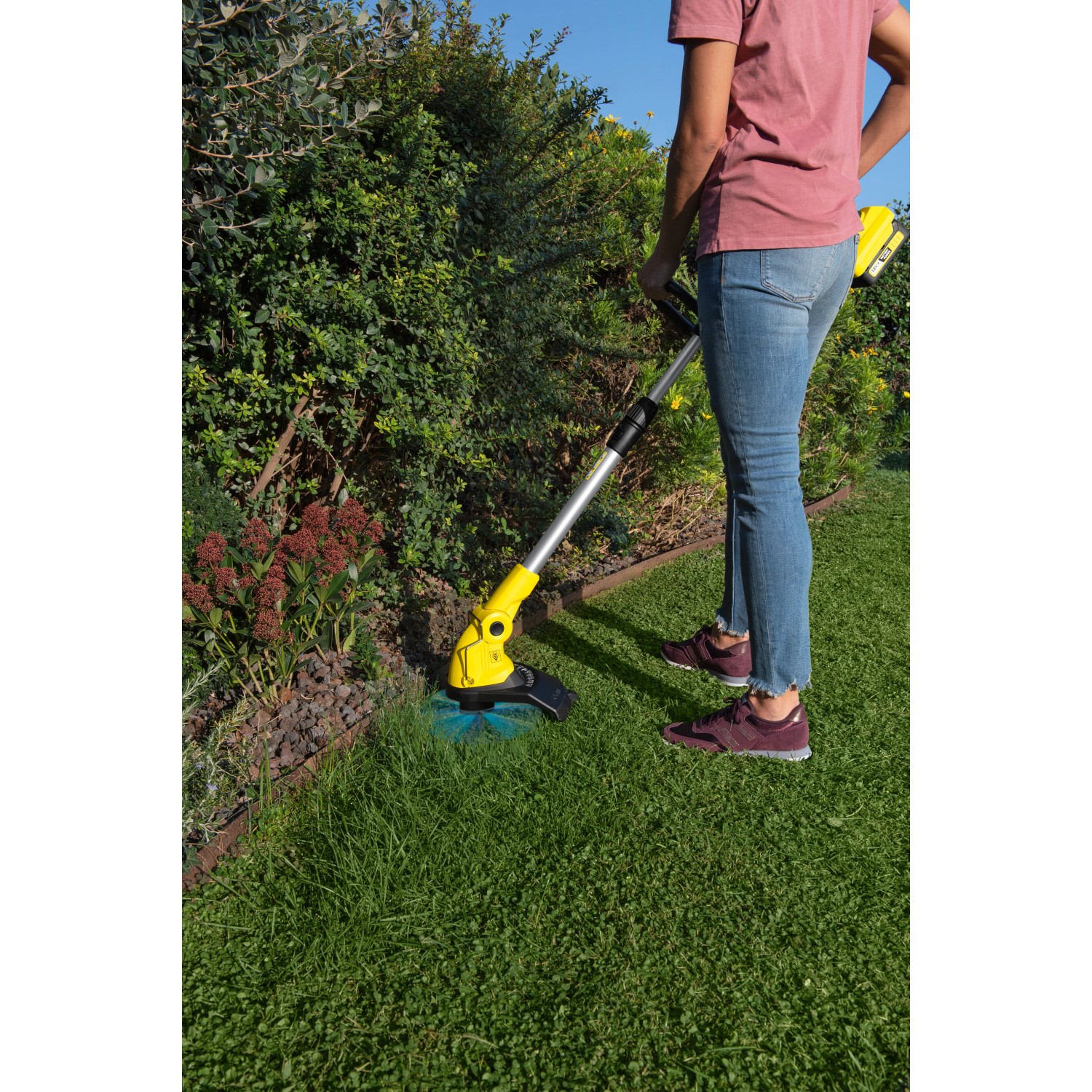 Frau trimmt Rasen mit gelbem Kärcher Akku-Rasentrimmer LTR 18-30. Akku-Trimmer für präzise Rasenkanten.