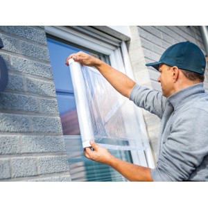 Mann bringt LUX Fensterschutzfolie am Fenster an. Klebefolie schützt vor Schmutz bei Renovierung.