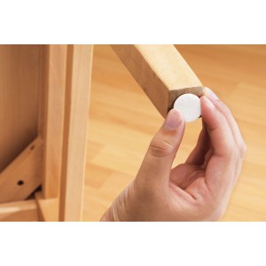 Anbringen eines weißen, selbstklebenden Filzgleiters an einem Stuhlbein zum Schutz des Bodens.